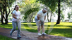 Joyful chubby girl outrunning obese man tired after jogging, exhausting workouts