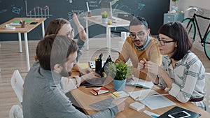 Joyful colleagues talking at desk in office then doing high-five and laughing