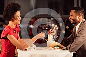 Joyful Couple Clinking Glasses Drinking Red Wine Sitting In Restaurant