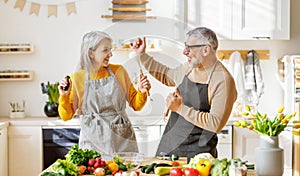 Joyful elderly couple have fun dancing and singing while cooking together in kitchen