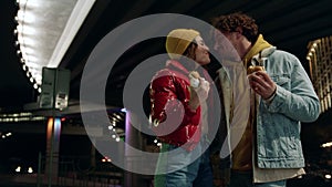 Joyful couple kissing on urban street. Man and woman enjoying snack food.