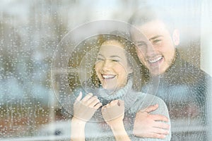 Joyful couple looking through a window a rainy day