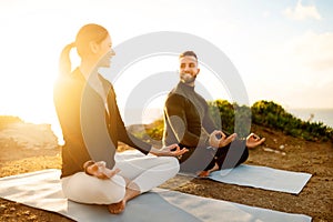 Joyful couple meditating on yoga mats at sunset