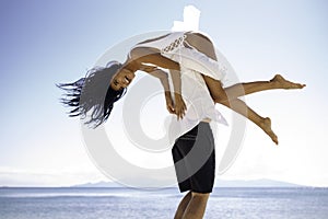 Joyful couple play on the beach, man holding a girlfriend on his shoulders,  on a clear sky, in summer time.