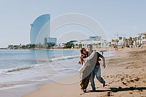 Joyful couple running hand in hand along a sunlit beach in Barcelona, Spain