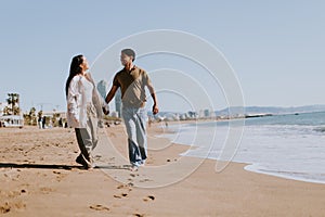 Joyful couple running hand in hand along a sunlit beach in Barcelona, Spain