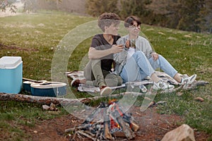 Joyful couple sitting on grass at picnic, talking and drinking tea or coffee. Tourism.