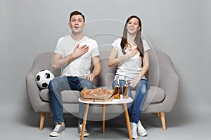 Joyful couple woman man football fans in white t-shirt cheer up support favorite team, sing hymn with hand on chest