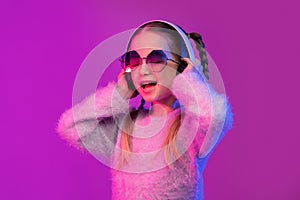 Joyful cute little girl using wireless headphones in neon light