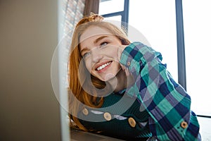 Joyful cute woman watching on monitor of laptop and laughing