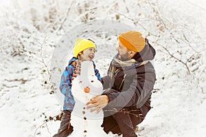 Joyful dad and son enjoying building a snowman.