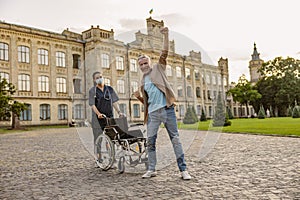 Joyful disabled handicapped mature man can walk again. Recovering patient standing up from his wheelchair, young nurse