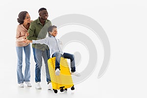 Joyful Diverse Parents Riding Son On Travel Suitcase, White Background