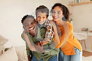 Joyful Diverse Parents And Their Son Embracing Posing At Home
