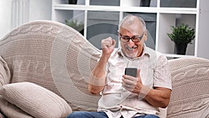 Joyful elderly 60s man look at smartphone celebrating victory success. 4k Dragon RED camera