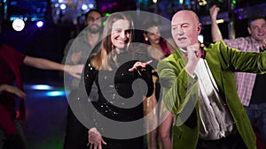 Joyful elderly Caucasian man and young woman dancing in night club. Positive people of different ages resting in the