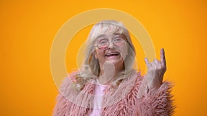 Joyful elderly lady in funny pink clothes making rocker gesture, positiveness
