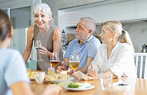 Joyful elderly women and man chatting and drinking at kitchen table