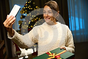 Joyful european woman taking selfie on smartphone with gift box during Christmas