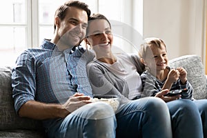 Joyful family couple cuddling son, watching tv show.