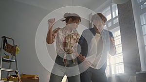 Joyful family enjoying improvement of apartment. Happy couple dancing indoors.