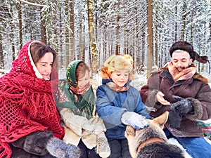 Joyful family ethnic dress with shawls and earflap hats and dog in winter forest in carnival Maslenitsa in Russia