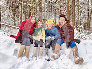 Joyful family ethnic dress with shawls and earflap hats in a winter forest in carnival Maslenitsa in Russia. Tourists in