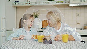 Joyful family granddaughter and grandmother having breakfast at home talking laughing