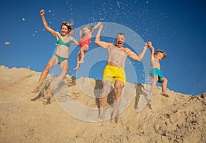 A joyful family leaping from sandy ridge against clear blue sky