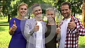 Joyful family members enjoying weekend in park and showing thumbs up into camera