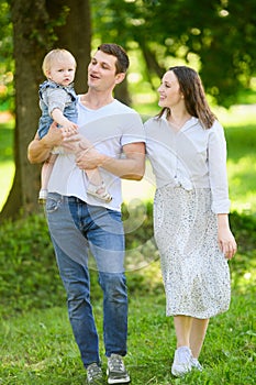 Joyful family walks in the park, a loving father holds a smiling child in his arms, laughs, a happy mom walks nearby.