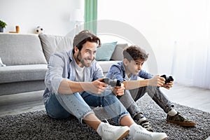 Joyful father and son competing in online video games, using joysticks, having fun at home.