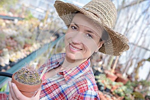Joyful female gardener holding cactus in greenhouse photo