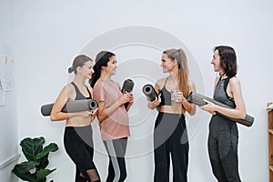 Joyful friendly women socialising at yoga club, holding rolled mats under arm