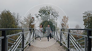 Joyful friends and athletes jog on a summer park bridge, as a sporty couple runs side by side. Engaged in outdoor