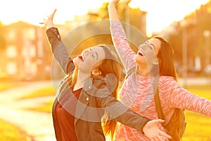 Joyful friends joking raising arms at sunset