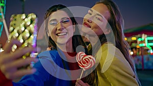 Joyful friends making selfie at night luna park closeup. Happy girls having fun