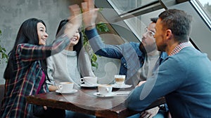 Joyful friends male and female chatting laughing and doing high-five in cozy cafe