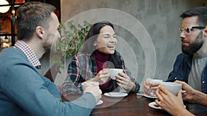 Joyful friends male and female talking and drinking coffee at table in cafe