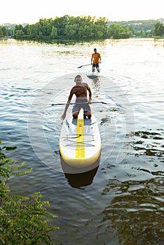 Joyful friends paddling on a SUP boards to the shore