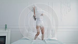 Joyful girl dancing on bed with pillow