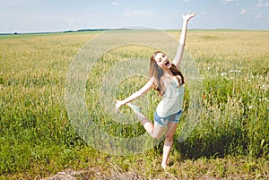 Joyful girl in green field with open arms dancing