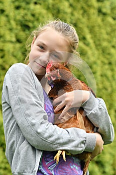 A joyful girl holds a chicken in her hands and hugs her