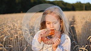 Joyful girl holds a fresh bun in a wheat field, happiness.