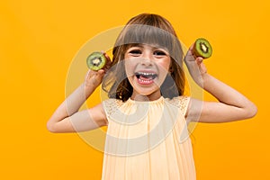 Joyful girl holds kiwi on a yellow background