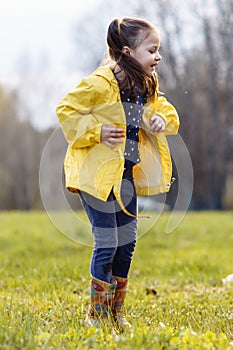 Joyful girl jumping up while standing in puddle on lawn, looking down with carefree expression, enjoying fall day.