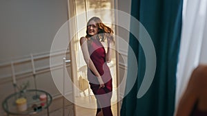 Joyful girl looking mirror trying romantic dress at home. Smiling happy woman