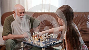 Joyful girl rejoicing clapping shaking hands with senior man playing chess indoors. Happy relaxed Caucasian