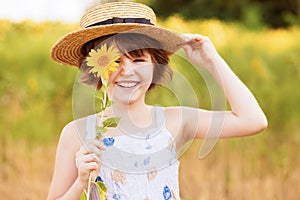 Joyful girl smiling and covering face with sunflower in field