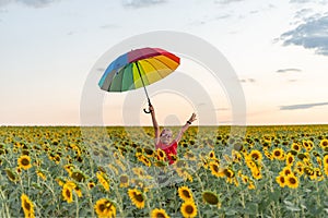 A joyful girl in sunglasses holds a colored umbrella at the top in a field of sunflowers